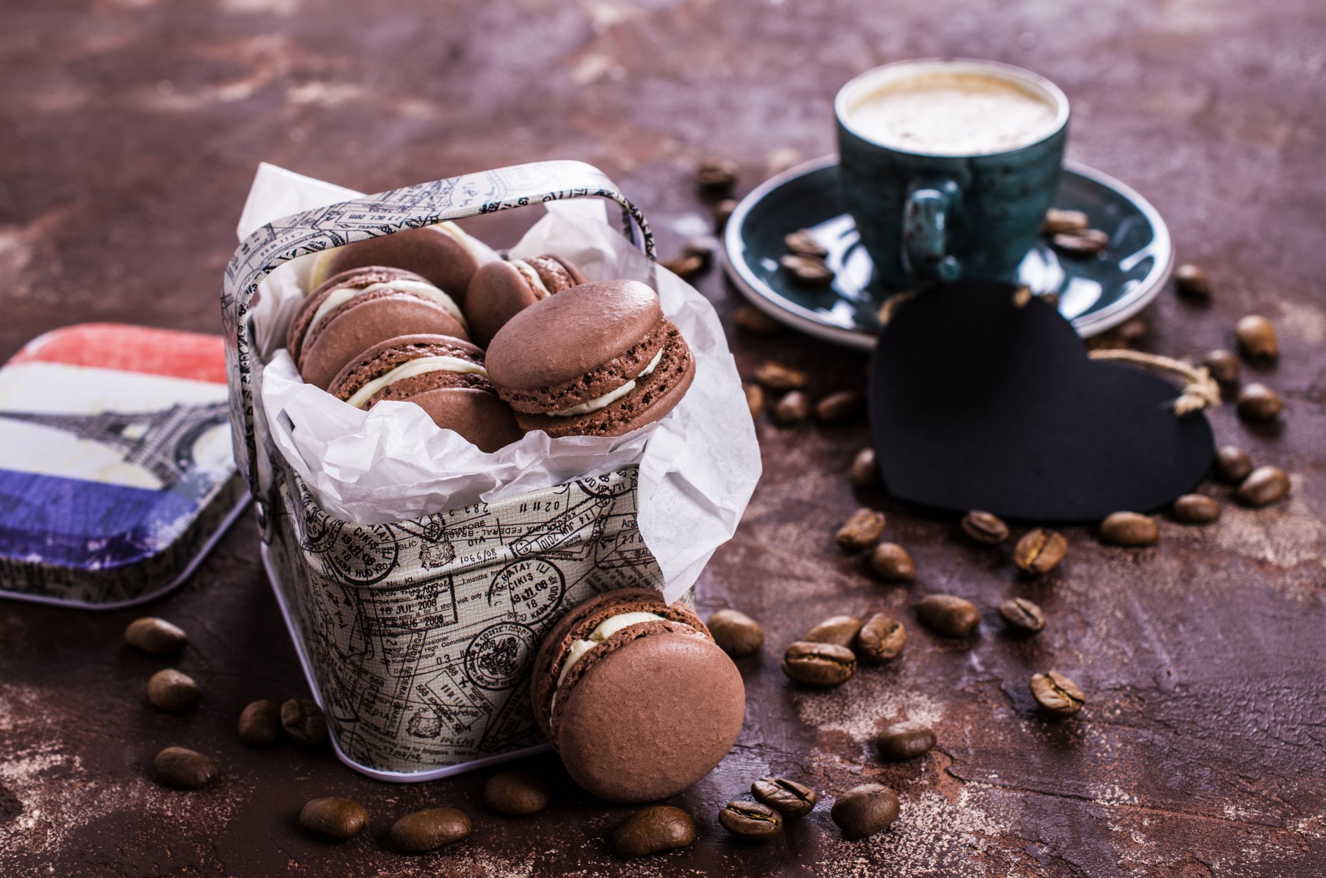 A 4K Ultra HD still life image featuring coffee beans, chocolate macarons in a decorative tin, and a cup of coffee on a rustic wooden surface.
