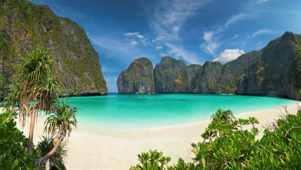Turquoise waters gently lap the white sandy beach of Phi Phi Island, Thailand, surrounded by dramatic limestone cliffs under a bright blue sky.