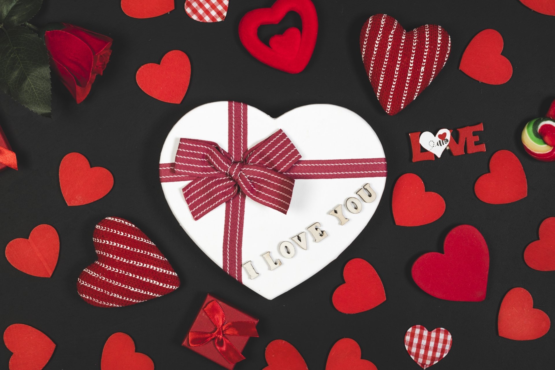 A romantic Valentine's Day 4K UHD wallpaper featuring a heart-shaped gift box with a bow, surrounded by red and patterned hearts on a dark background.