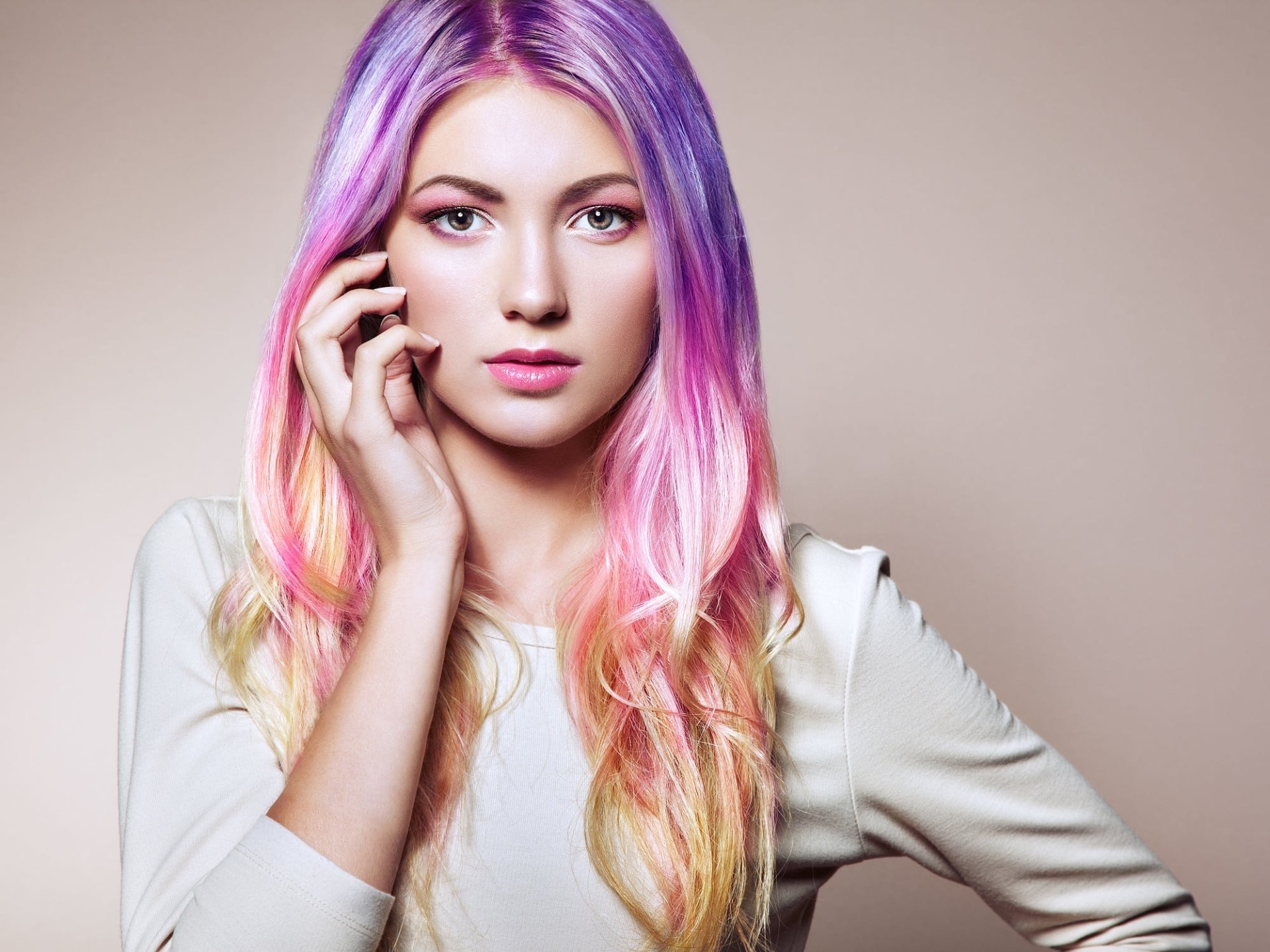 Portrait of a model with long pastel pink and purple hair, wearing lipstick, posing confidently against a neutral background in HD, suitable as a PC desktop wallpaper.