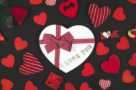 A romantic Valentine's Day 4K UHD wallpaper featuring a heart-shaped gift box with a bow, surrounded by red and patterned hearts on a dark background.