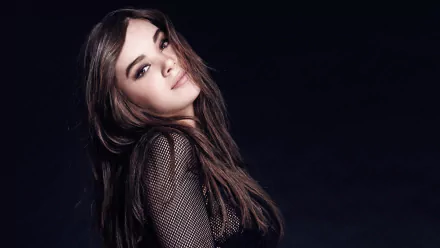 HD desktop wallpaper featuring American singer and actress Hailee Steinfeld with long brunette hair and brown eyes, wearing a black outfit against a dark background.