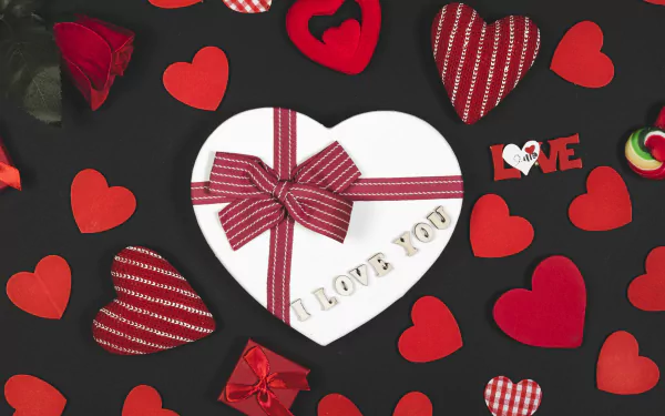 A romantic Valentine's Day 4K UHD wallpaper featuring a heart-shaped gift box with a bow, surrounded by red and patterned hearts on a dark background.