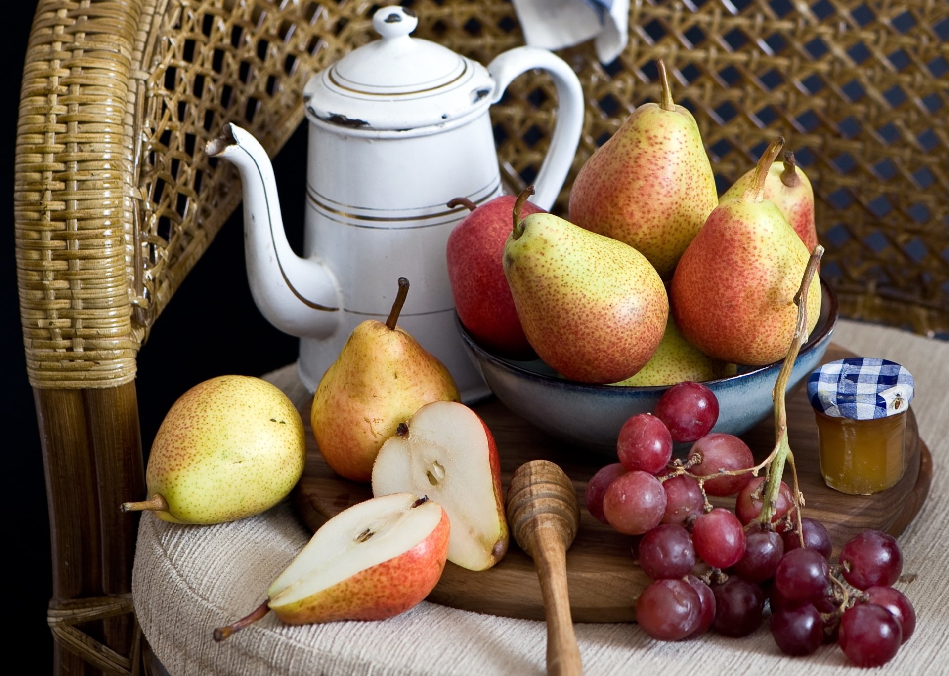 2K Quad HD PC desktop wallpaper still life: white teapot beside bowl of pears, sliced pear, red grapes, honey jar and dipper on woven chair — fruit-themed food background.