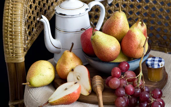 2K Quad HD PC desktop wallpaper still life: white teapot beside bowl of pears, sliced pear, red grapes, honey jar and dipper on woven chair — fruit-themed food background.