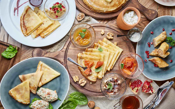 HD desktop wallpaper featuring a still life of assorted crêpes with various fillings and toppings, arranged on plates and wooden boards for a vibrant food display.