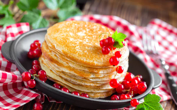 Golden crêpe stack garnished with red currants and berry sprigs on a plate over a gingham cloth — 5K Ultra HD PC desktop wallpaper background.