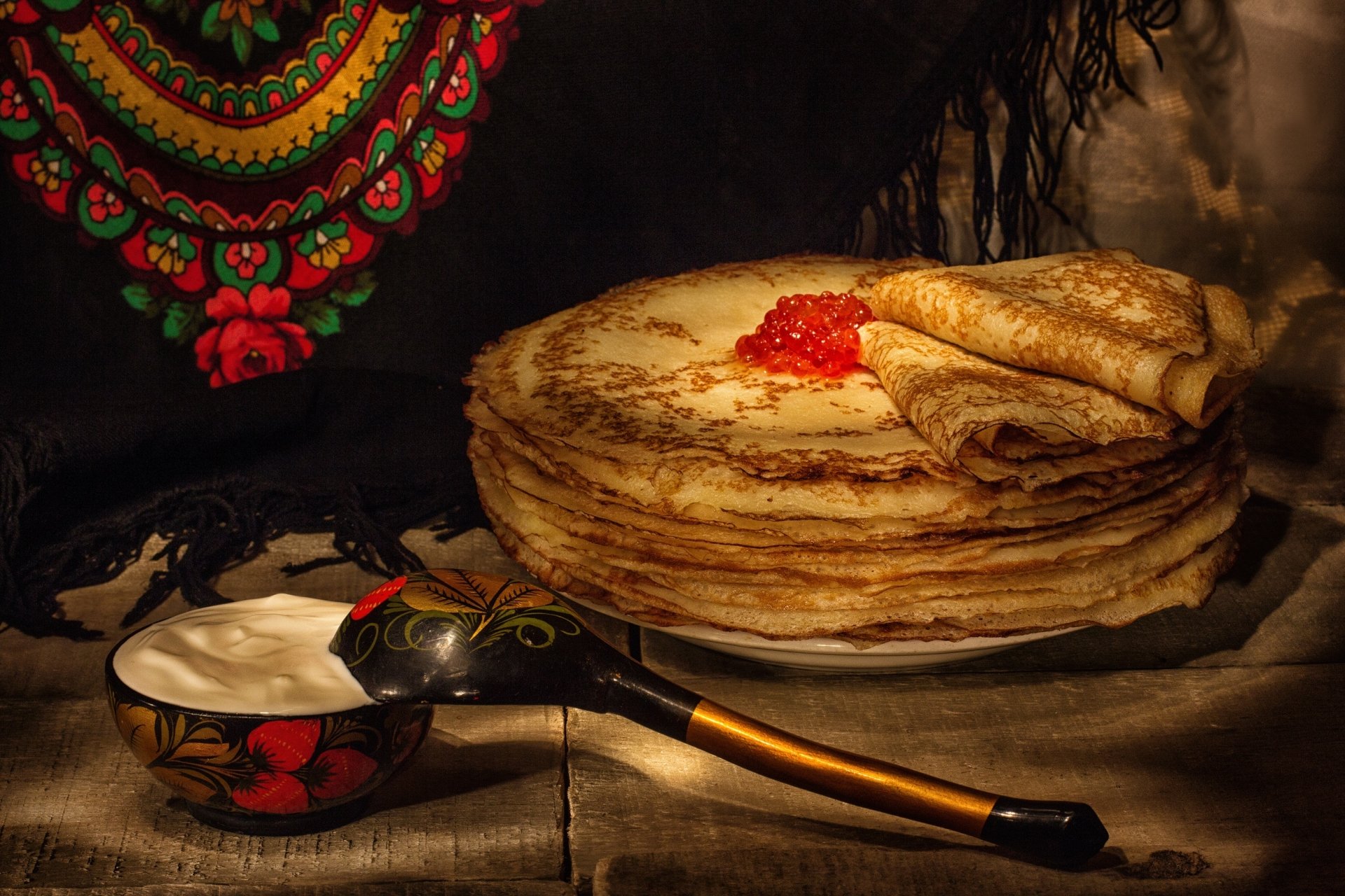 HD desktop wallpaper showcasing a still life of golden crêpes topped with red caviar, accompanied by a traditional wooden spoon and bowl, set against a dark, textured background.