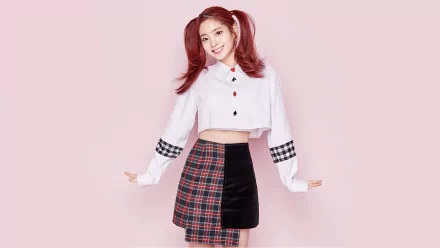 HD wallpaper of Dahyun from K-pop group Twice, smiling with red hair in ponytails, wearing a white cropped shirt and a black-and-red plaid skirt against a pink background.