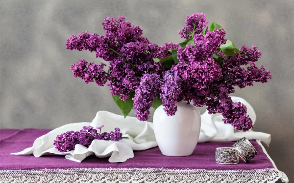 A vibrant lilac bouquet in a white vase on a purple lace cloth with a gray background, captured in a high-resolution 4K Ultra HD still life photography.