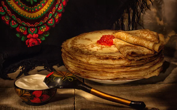 HD desktop wallpaper showcasing a still life of golden crêpes topped with red caviar, accompanied by a traditional wooden spoon and bowl, set against a dark, textured background.