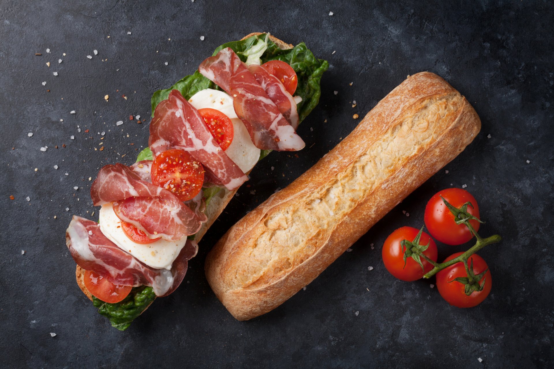 4K Ultra HD desktop wallpaper featuring a fresh sandwich with meat, tomato, and bread on a dark textured background alongside cherry tomatoes.