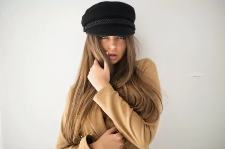 Brunette woman model with long hair and blue eyes wearing a tan coat and black cap, posed against a white background — 2K Quad HD PC desktop wallpaper