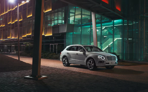 Silver Bentley Bentayga SUV parked at night in front of a modern glass building, captured in stunning 4K Ultra HD for a PC desktop background.