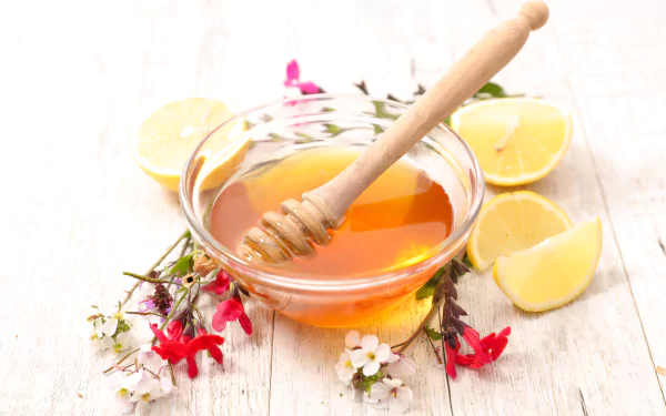 8K Ultra HD still life of fresh lemon slices and a glass bowl of honey with a wooden dipper, accented by small red and white flowers on a light wooden surface.