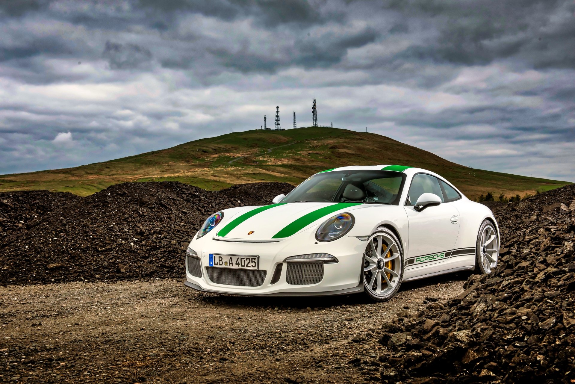 White Porsche 911 Turbo sports car with green racing stripes is parked on a rugged terrain under a cloudy sky in this 4K Ultra HD desktop wallpaper.
