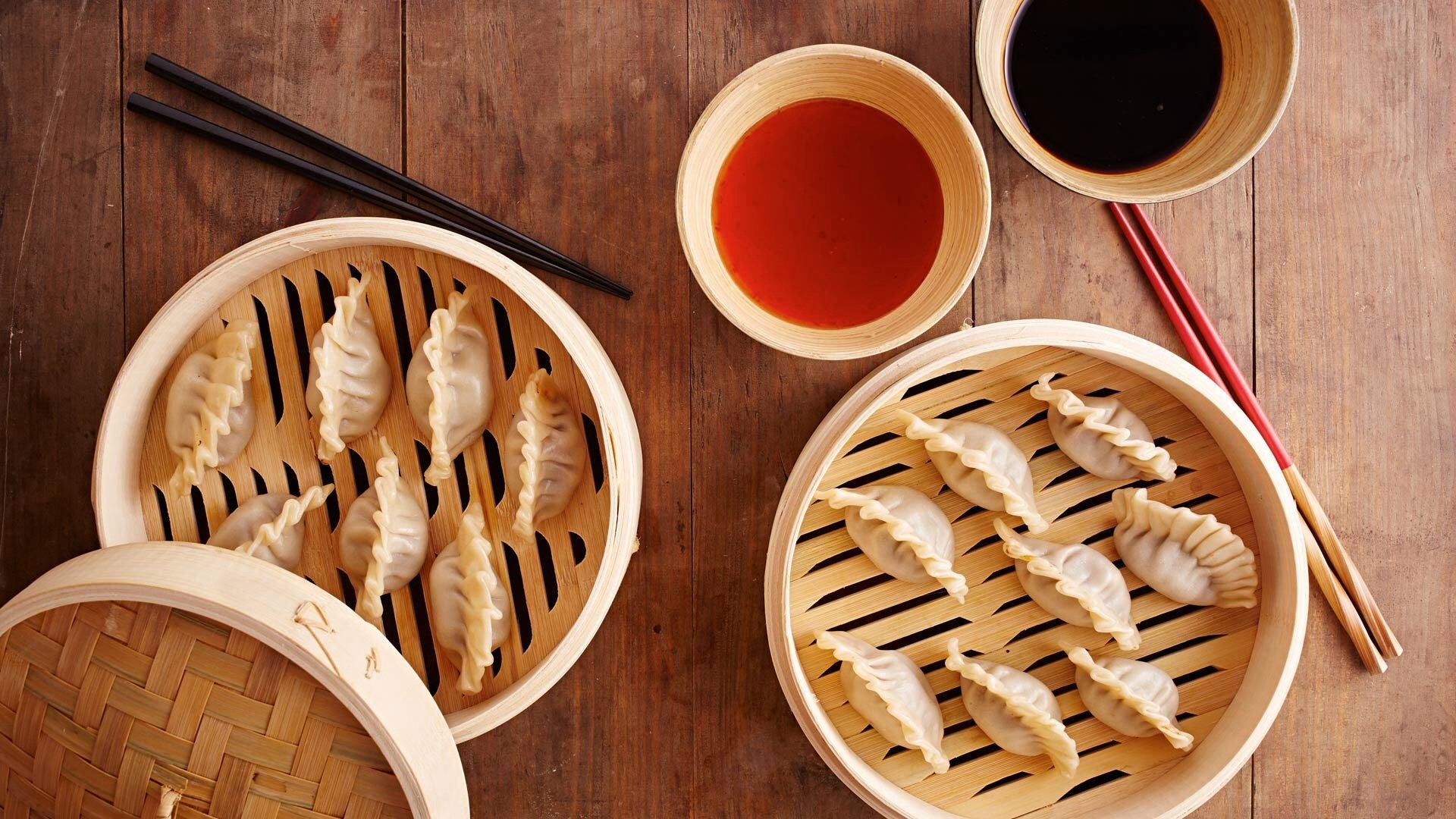 HD PC desktop wallpaper/background: bamboo steamers of Chinese potstickers with dipping sauces and chopsticks arranged on a warm wooden table.