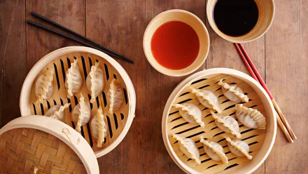 HD PC desktop wallpaper/background: bamboo steamers of Chinese potstickers with dipping sauces and chopsticks arranged on a warm wooden table.