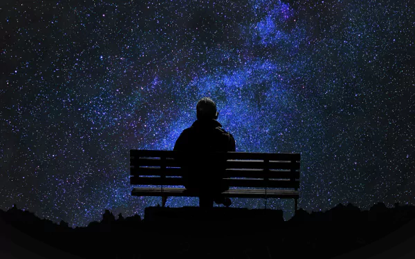 A man sits alone on a bench under a starry night sky, gazing at the vast expanse of twinkling stars. This HD desktop wallpaper evokes feelings of solitude and wonder.