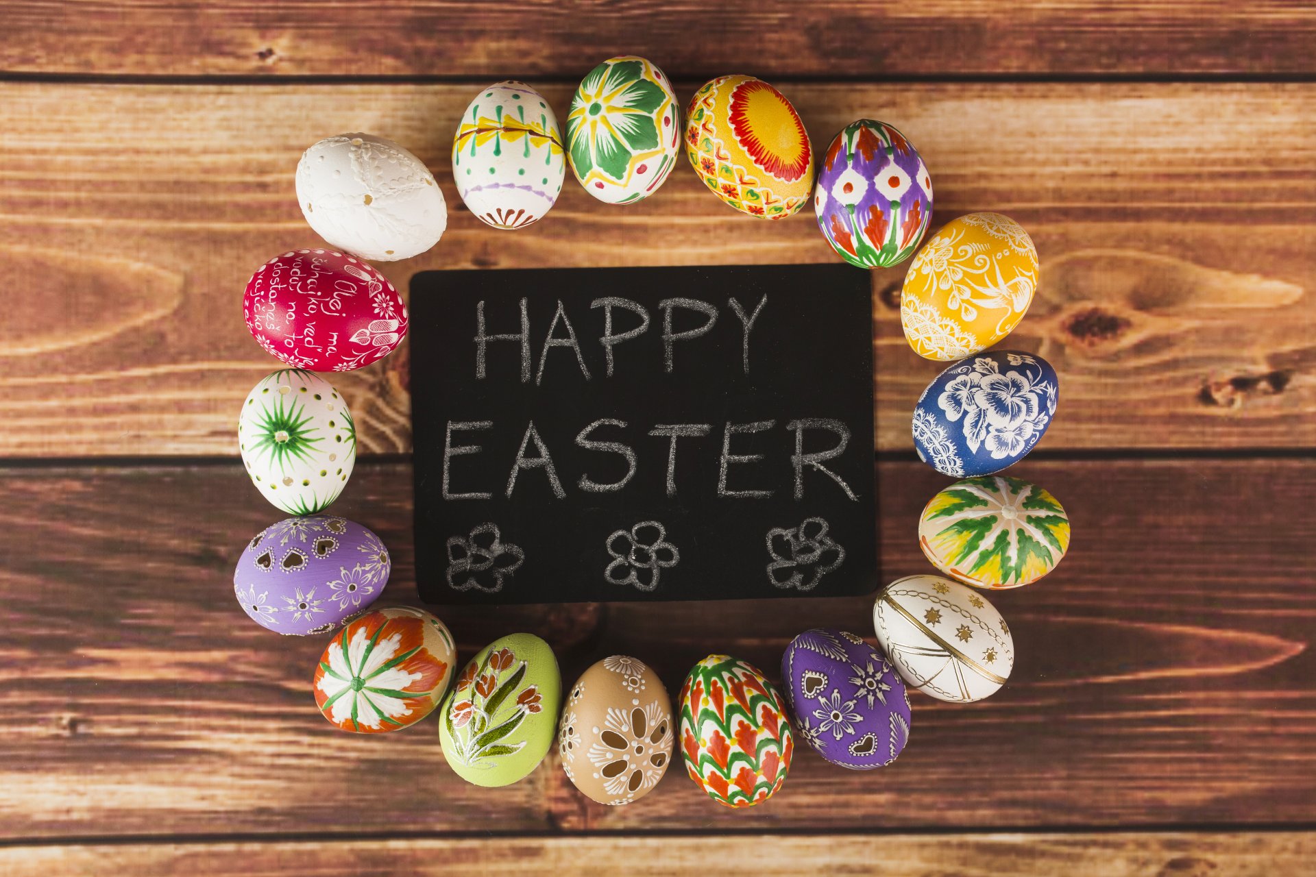 Colorful Easter eggs encircle a chalkboard with Happy Easter written on it, set on a wooden background in this vibrant 4K Ultra HD holiday wallpaper.