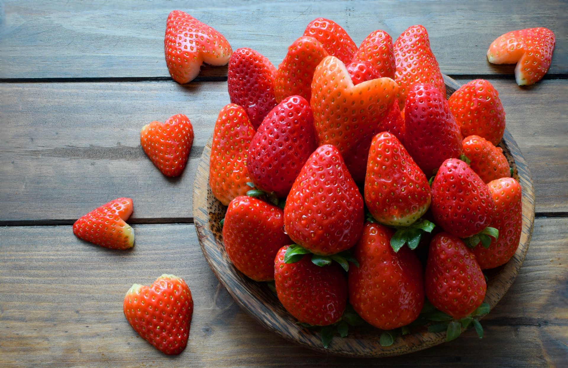 A vibrant 4K Ultra HD desktop wallpaper featuring fresh, heart-shaped strawberries arranged in a bowl and scattered on a wooden surface.