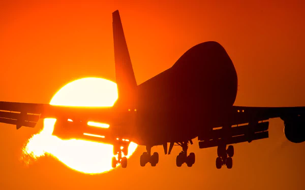 Silhouette of a Boeing 747 passenger aircraft descending toward the glowing sun at sunset — HD PC desktop wallpaper background.