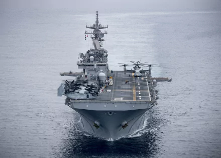 Front view of the USS Essex (LHD 2) amphibious assault ship with helicopters on deck, sailing through calm waters.