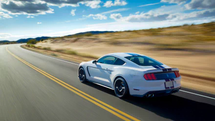 White Ford Mustang Shelby GT350 muscle car driving on an open road under a partly cloudy sky, captured as an HD PC desktop wallpaper and background.
