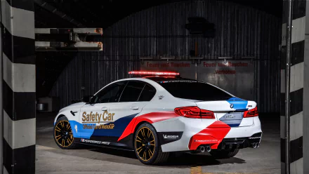 BMW M5 MotoGP Safety Car: white BMW M5 with red-blue livery, rooftop lightbar and gold wheels, presented as a 5K Ultra HD PC desktop wallpaper background.