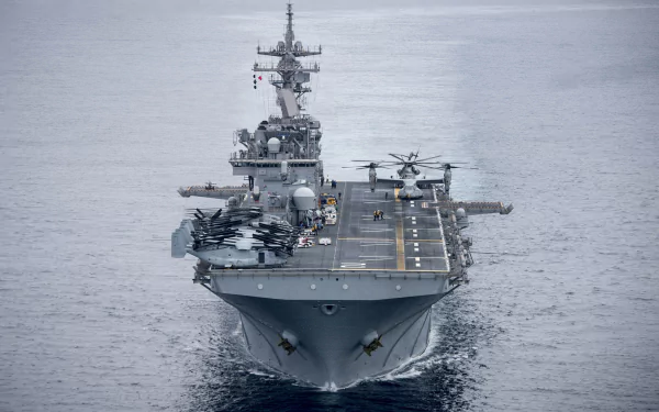 Front view of the USS Essex (LHD 2) amphibious assault ship with helicopters on deck, sailing through calm waters.