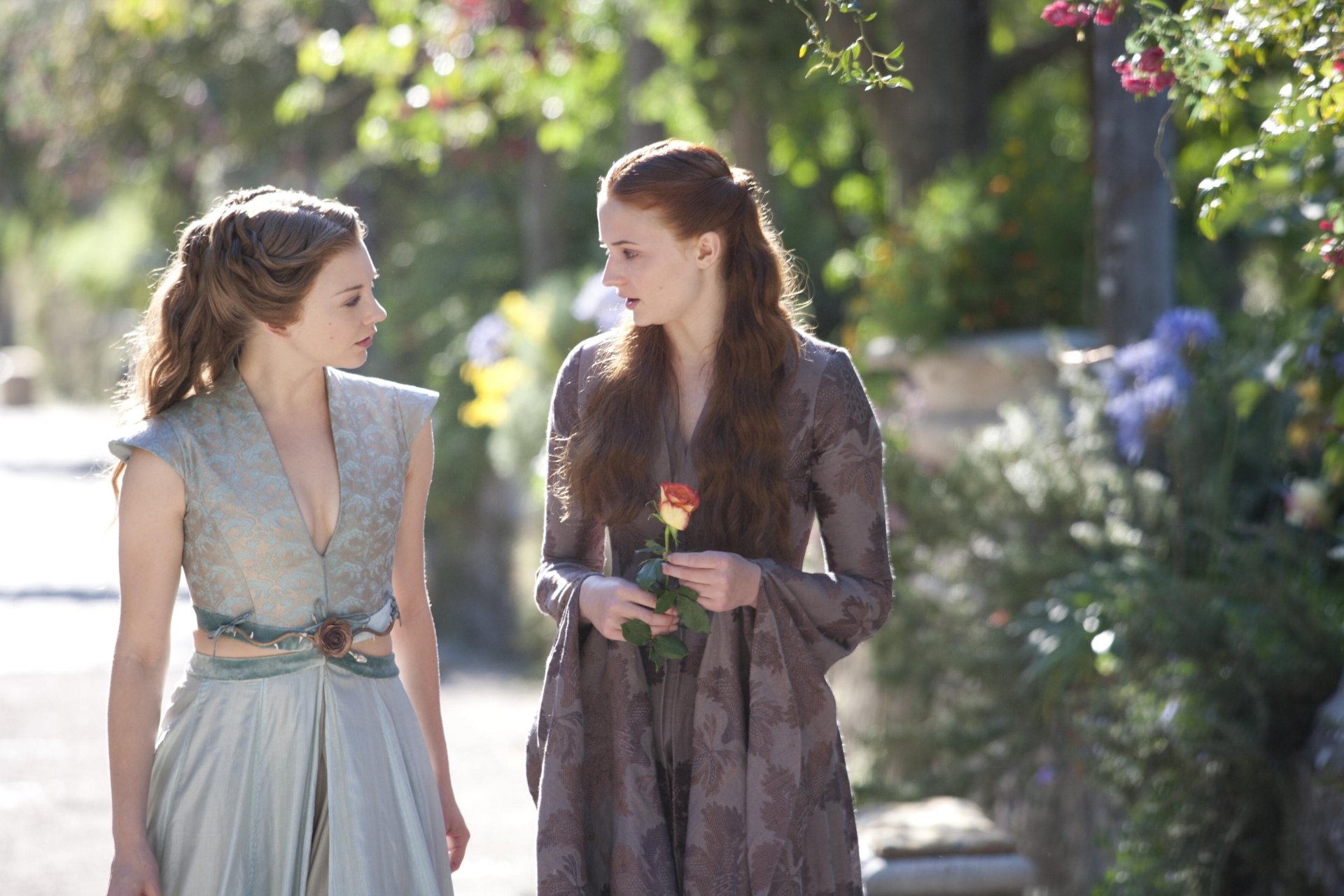 HD desktop wallpaper featuring Sophie Turner as Sansa Stark and Natalie Dormer as Margaery Tyrell from the TV show Game of Thrones, walking in a sunlit garden.