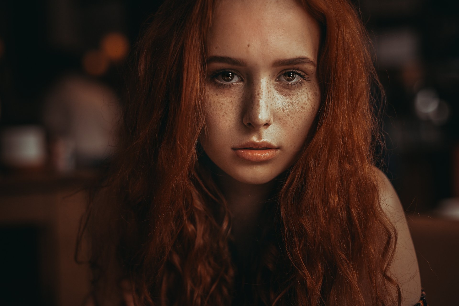 Close-up portrait of a freckled redhead woman model, face and intense gaze framed by long auburn hair — 4K Ultra HD PC desktop wallpaper and background.
