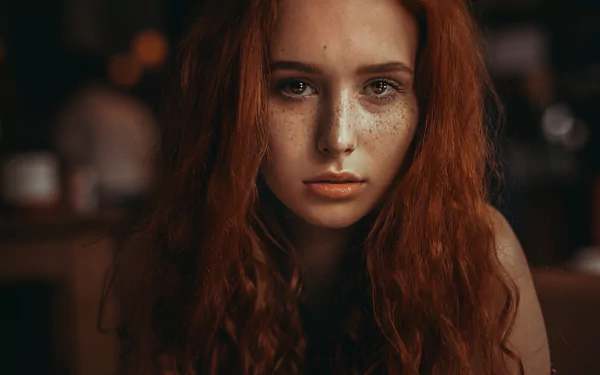 Close-up portrait of a freckled redhead woman model, face and intense gaze framed by long auburn hair — 4K Ultra HD PC desktop wallpaper and background.
