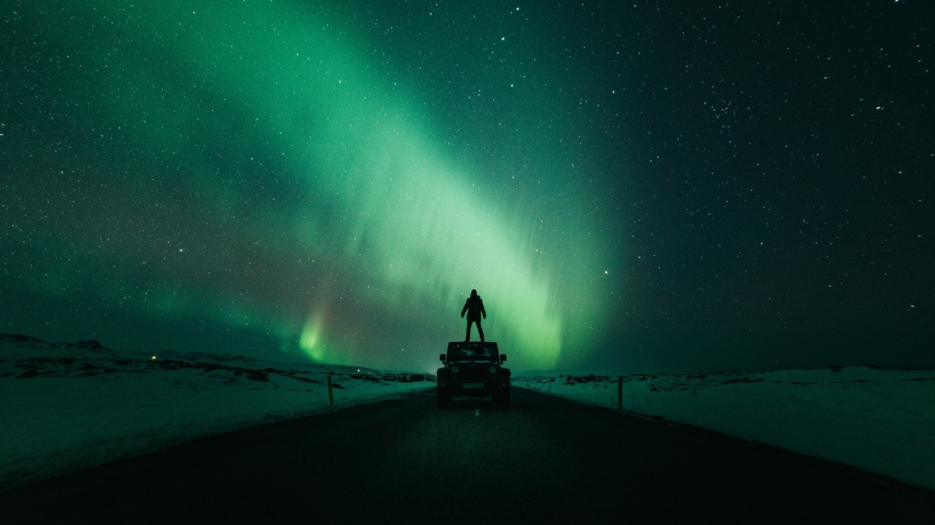 HD PC desktop wallpaper/background: silhouetted person standing on a vehicle beneath vivid green aurora borealis sweeping across a snowy night landscape — nature scene.