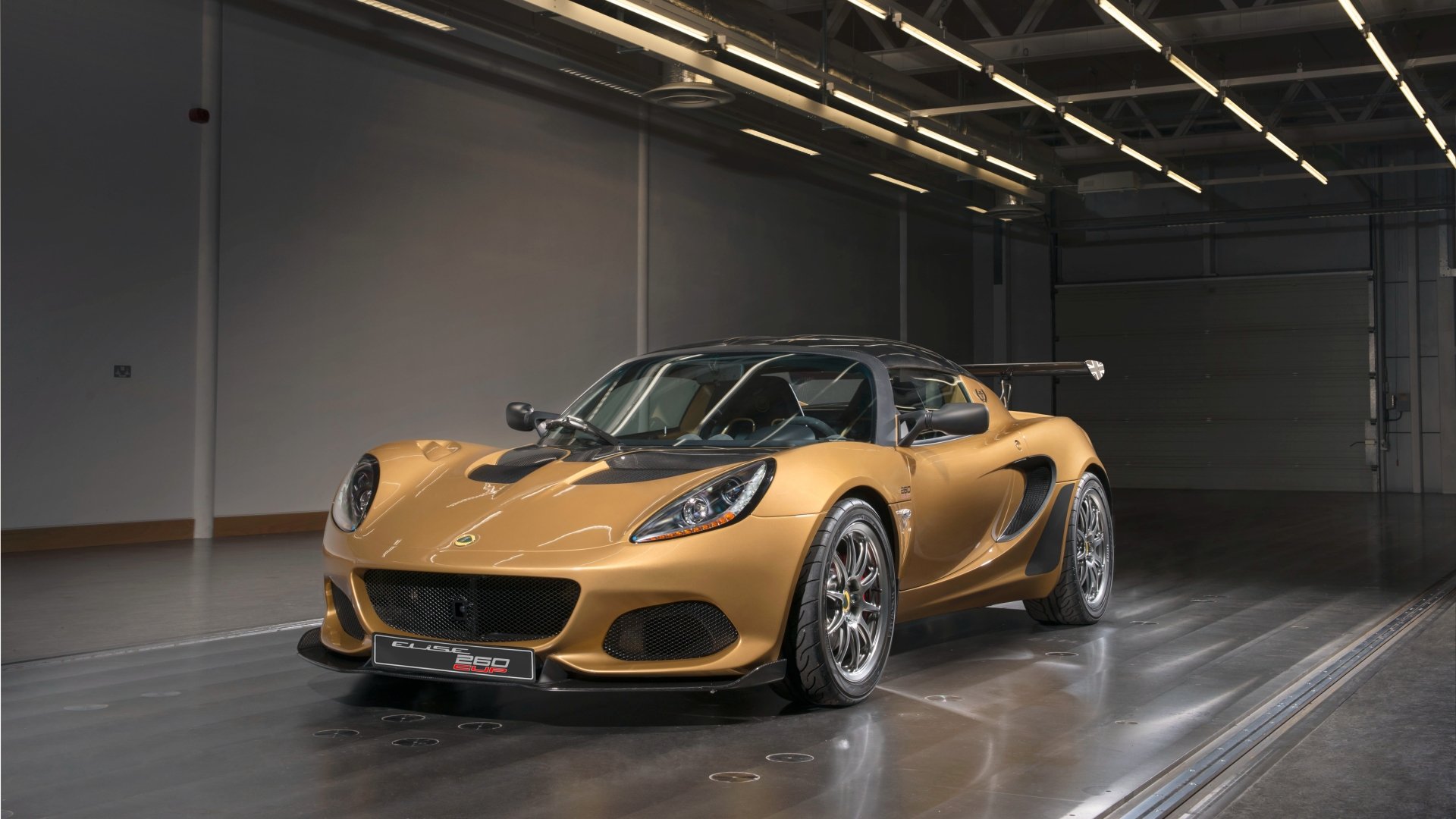 Gold Lotus Elise supercar parked in a glossy industrial garage, 4K Ultra HD PC desktop wallpaper of a Lotus (Car) sports vehicle.