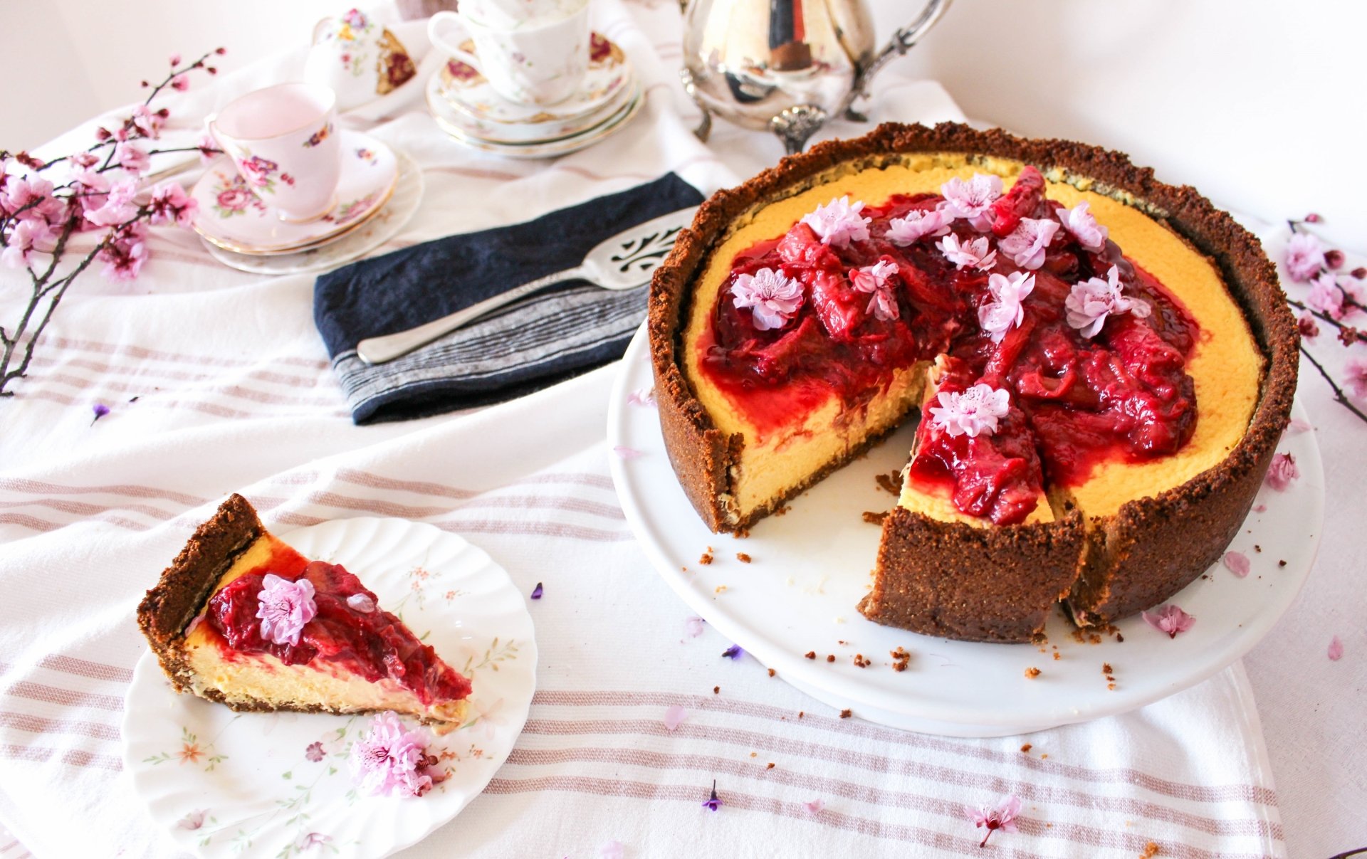 HD still life desktop wallpaper featuring a rich cheesecake topped with vibrant red berries and delicate edible flowers, set on an elegant table with silverware and floral accents.