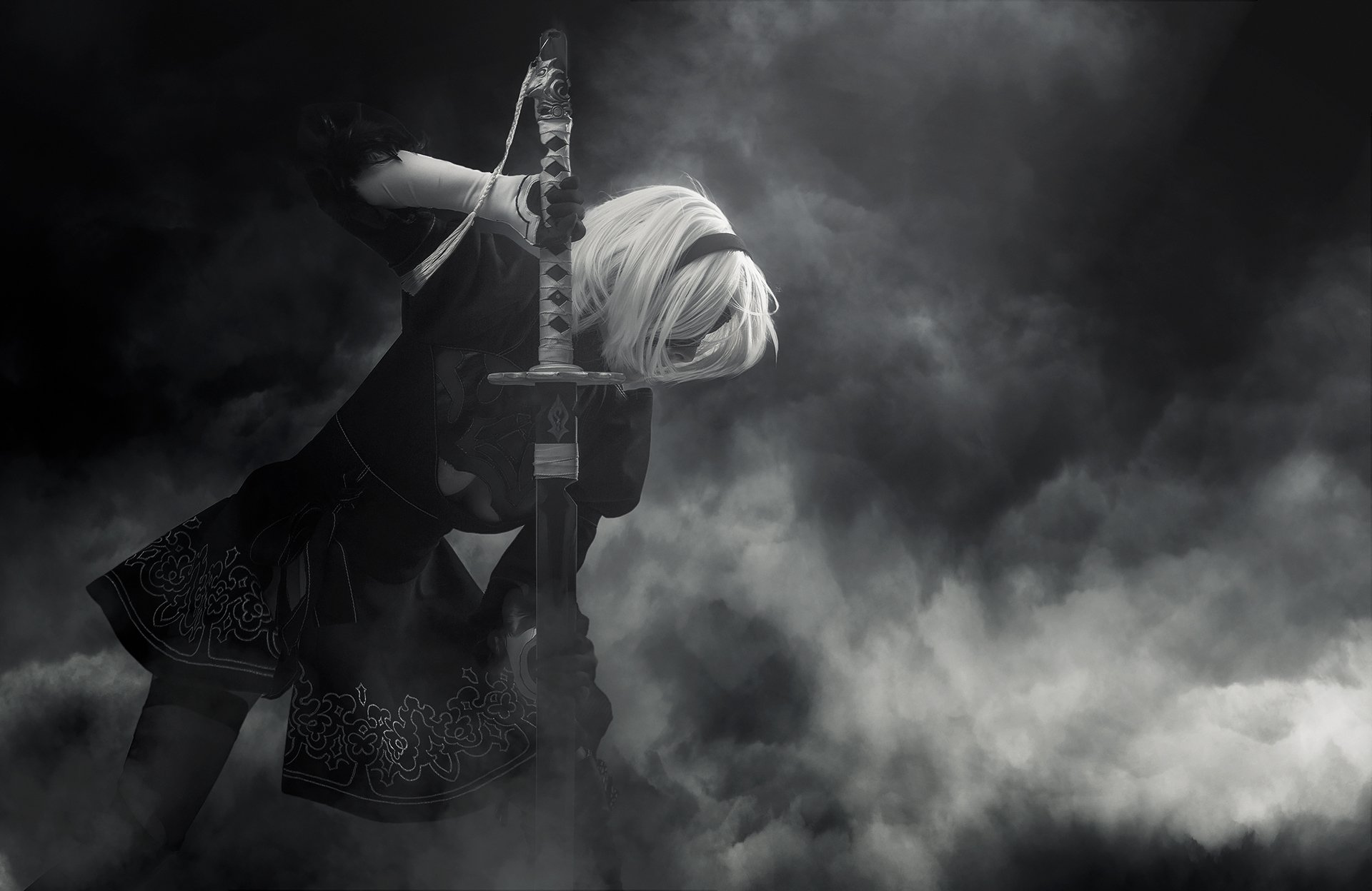 HD PC desktop wallpaper of a woman cosplaying 2B from NieR: Automata, kneeling with her sword amid swirling smoke in a moody monochrome scene.