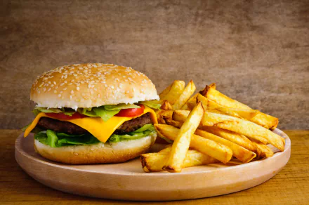 4K Ultra HD image of a cheeseburger with lettuce and tomato, served with a side of golden French fries on a wooden plate against a rustic background.