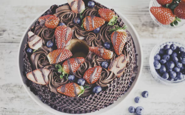 HD PC desktop wallpaper still life: chocolate pastry cake ring topped with strawberries, chocolate rosettes and bowls of blueberries, with a small bluebird accent.