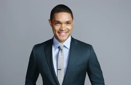 HD desktop wallpaper of a smiling man in a suit from The Daily Show with Trevor Noah against a grey background.