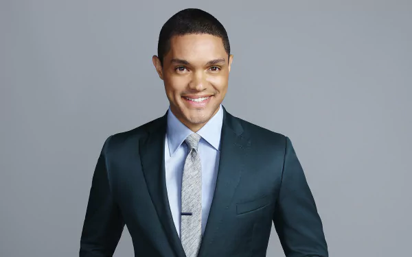 HD desktop wallpaper of a smiling man in a suit from The Daily Show with Trevor Noah against a grey background.
