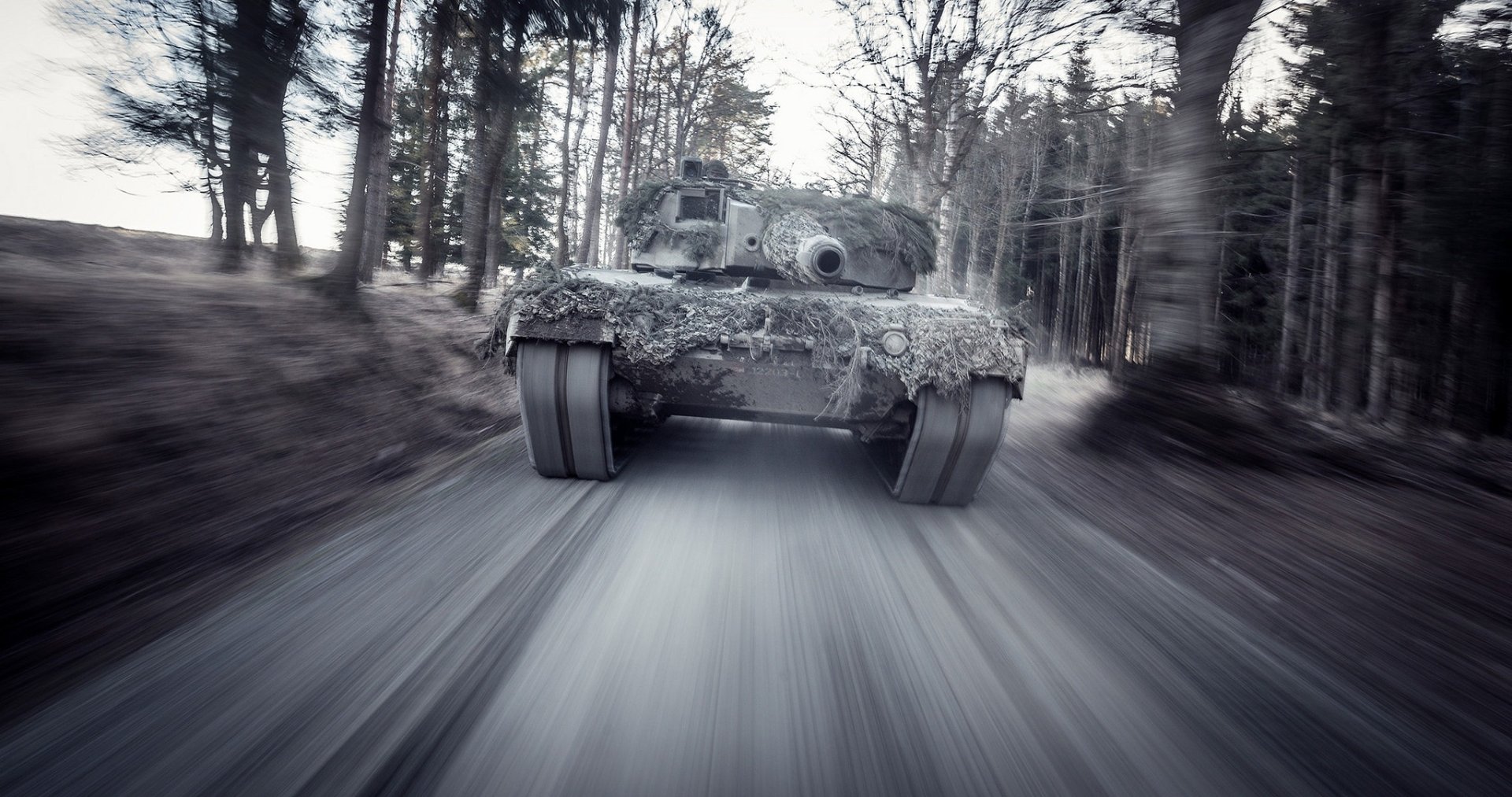 HD desktop wallpaper: a Leopard 2 military tank charging down a forest road with dramatic motion blur conveying speed and power.