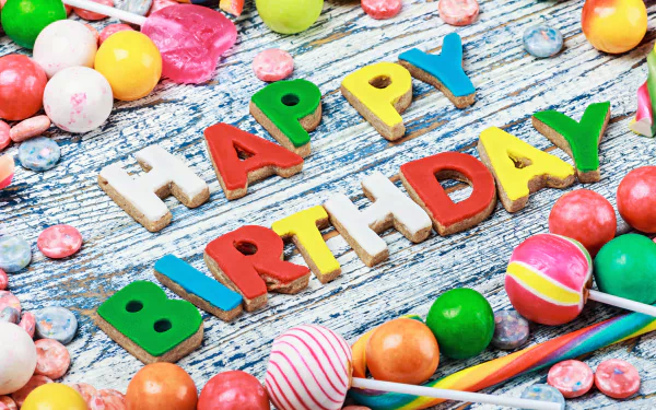 Colorful lollipops and assorted candy surround bright, bold letters spelling Happy Birthday on a wooden surface, featured as a 4K Ultra HD holiday-themed desktop wallpaper.