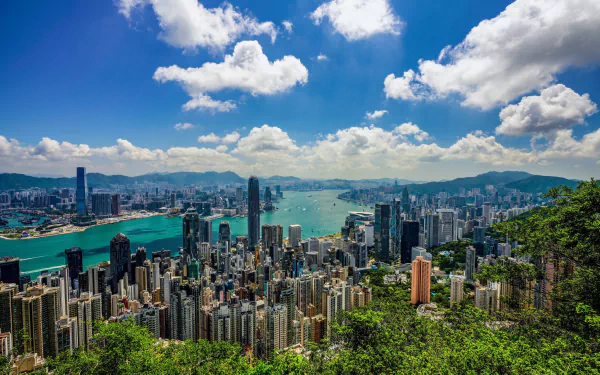 HD desktop wallpaper showing Hong Kong’s cityscape with numerous skyscrapers under a bright blue sky with scattered clouds, highlighting the man-made urban landscape in China.