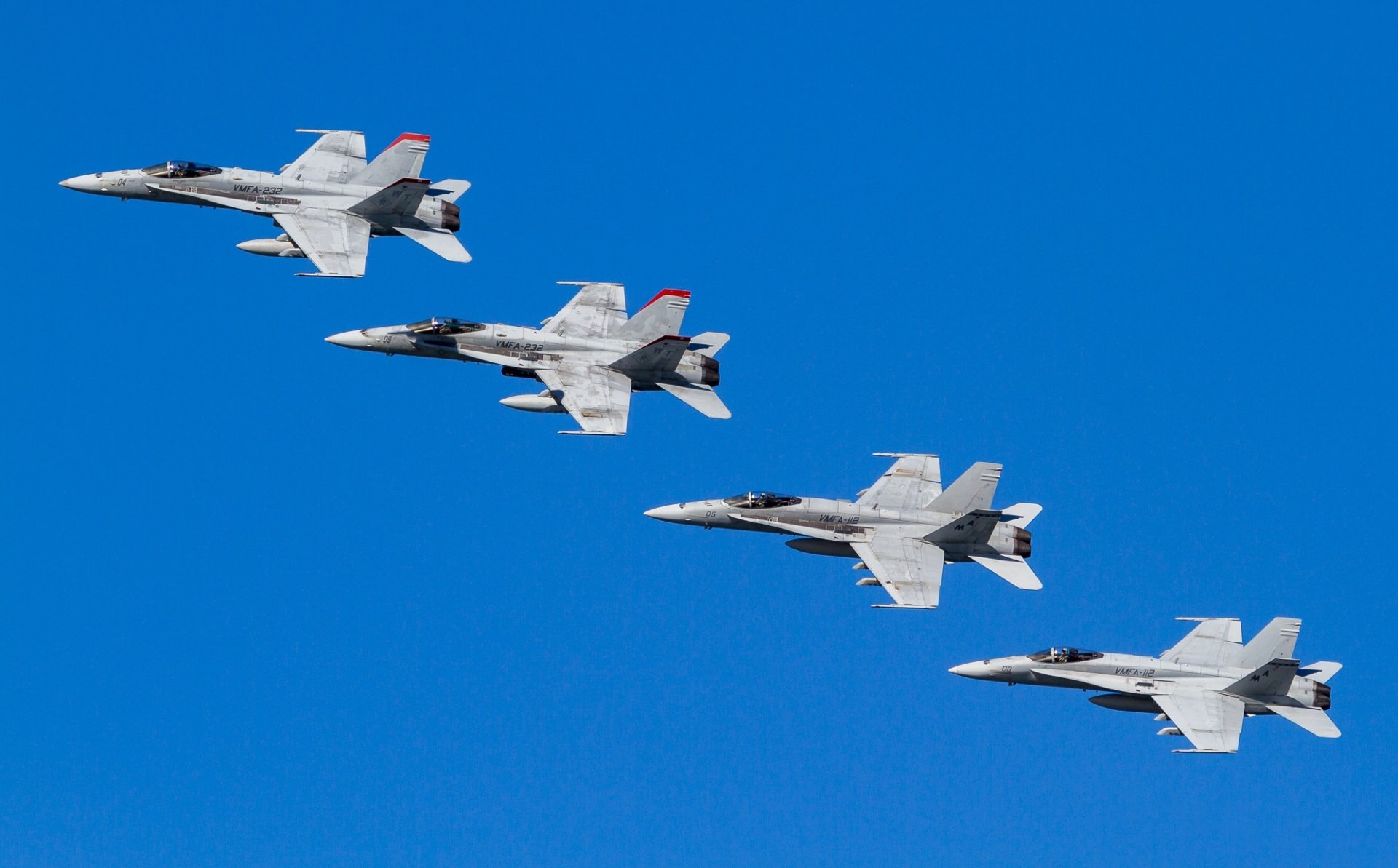 Four McDonnell Douglas F/A-18 Hornet jet fighter warplanes fly in formation against a clear blue sky in this HD military aircraft desktop wallpaper.