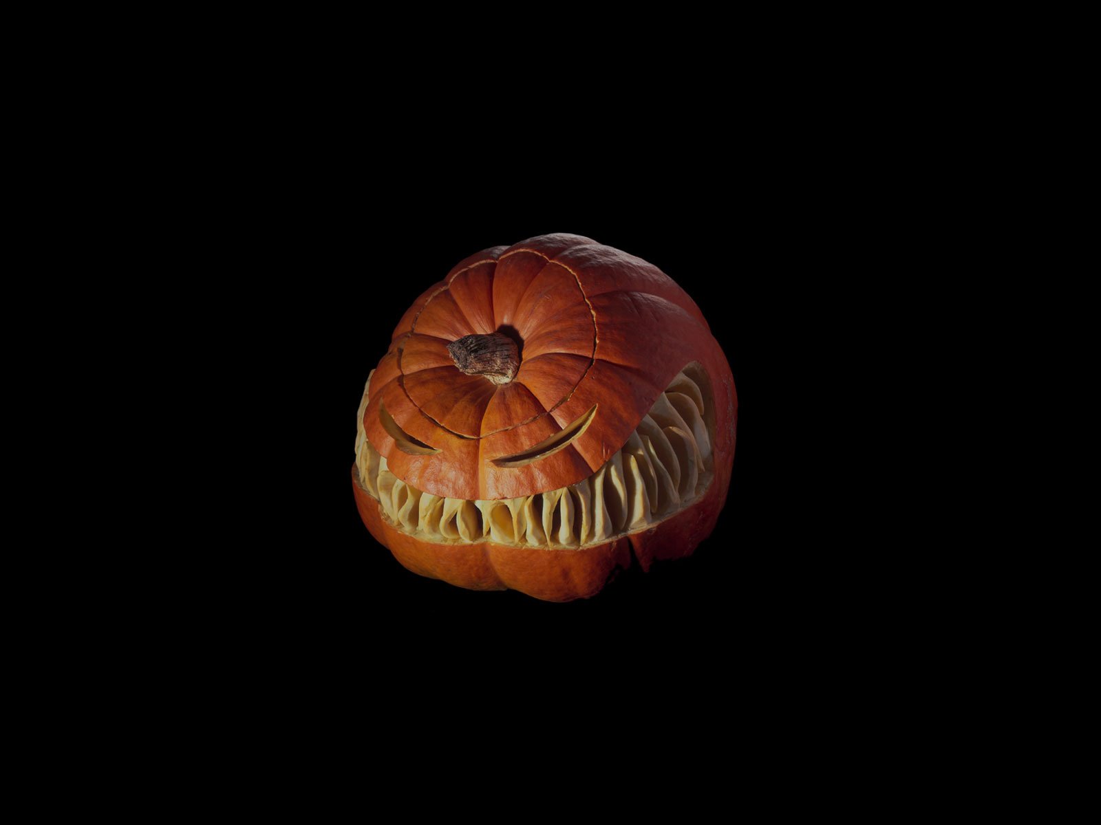 A carved pumpkin with a menacing grin against a black background, capturing the eerie essence of Halloween in a vibrant HD desktop wallpaper.