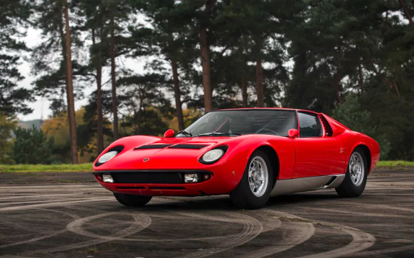 Red Lamborghini Miura supercar parked on a circular asphalt pattern, surrounded by tall trees in a serene outdoor setting. HD PC desktop wallpaper and background.