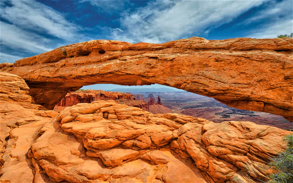 Mesa Arch in Utah framing a vast canyon and blue sky, warm sandstone foreground and distant peaks — nature scene; 2K Quad HD PC desktop wallpaper/background.
