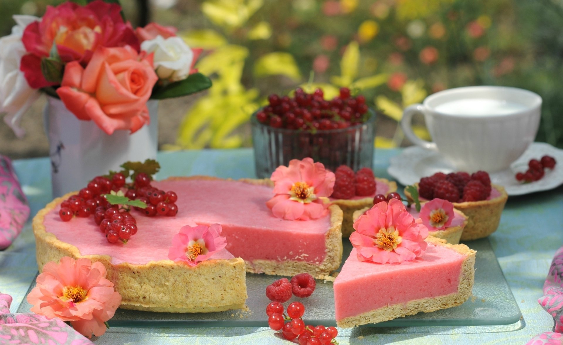 A vibrant still life HD desktop wallpaper featuring a pink currant dessert tart garnished with fresh currants and edible flowers, accompanied by a cup of tea and roses.