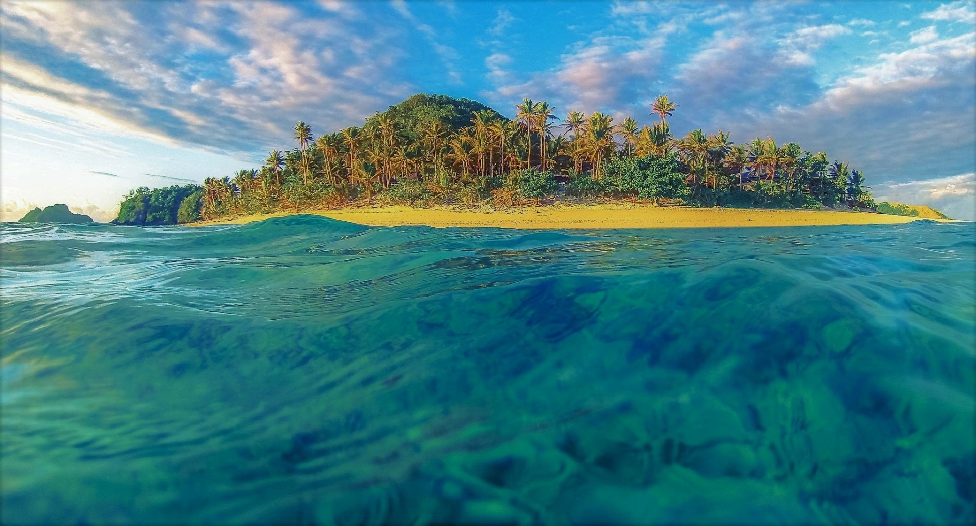 HD PC desktop wallpaper: turquoise ocean waves washing a tropical island shore, vivid sea and nature scenery beneath a bright blue sky.